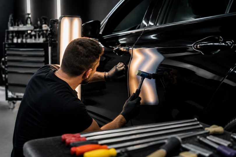 Técnico realizando martelinho de ouro em porta frontal de veículo estacionado em oficina de estética automotiva